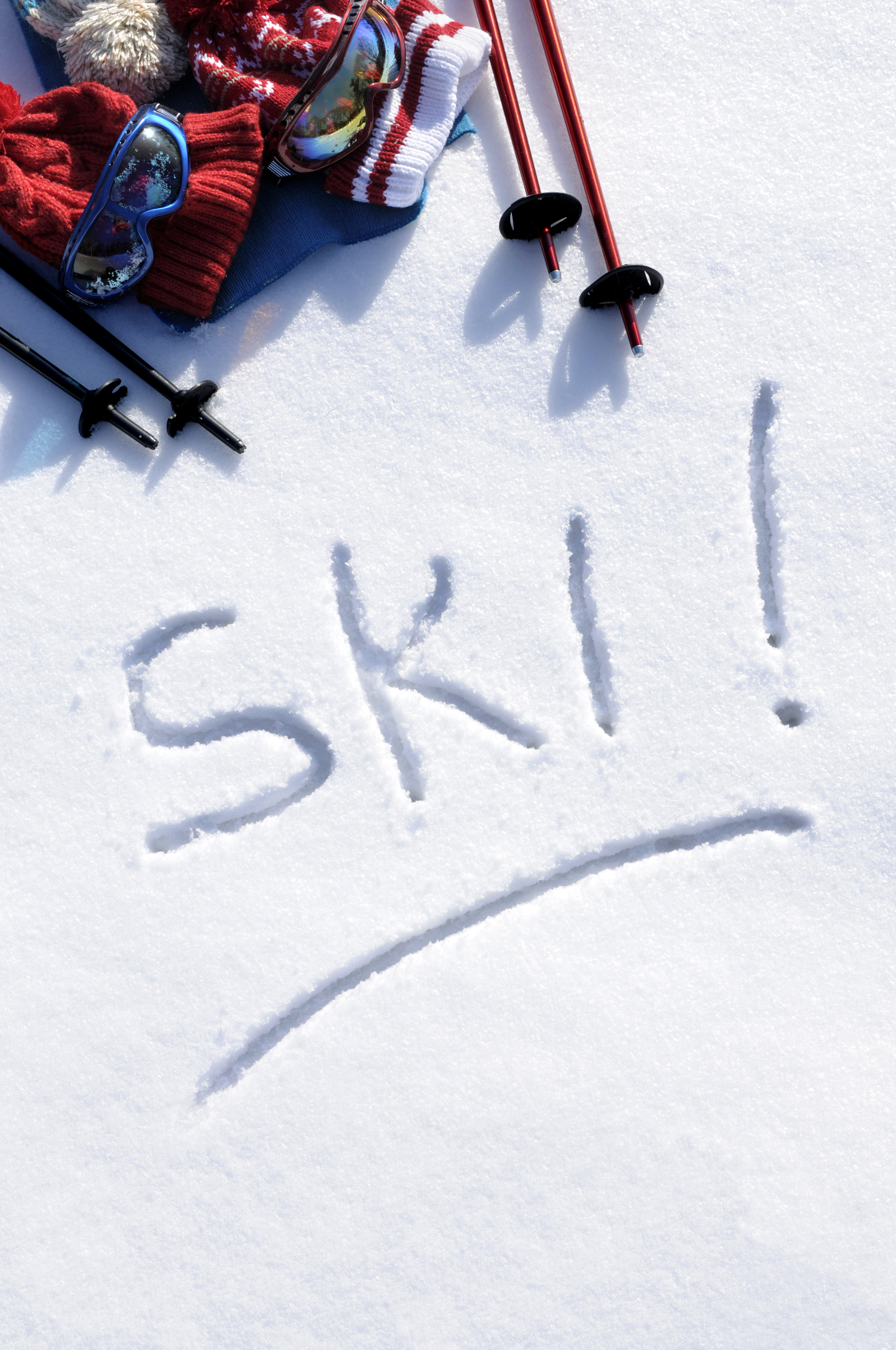 Ski goggles, hats and poles laid on snow beside the word &ldquo;SKI&rdquo;